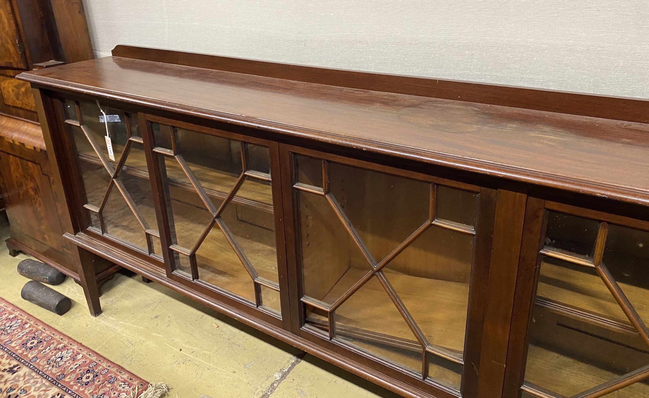 An Edwardian glazed mahogany dwarf bookcase, enclosed by six astragal glazed sliding doors, width 290cm, depth 34cm, height 94cm